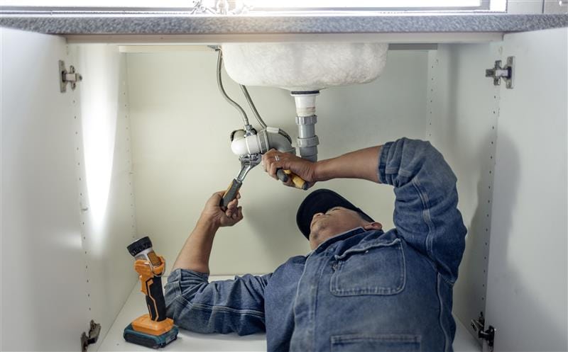 Plumber repairing pipes beneath a bathroom sink in Villa Rica