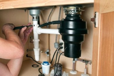Plumber repairing a garbage disposal beneath a kitchen sink in Villa Rica