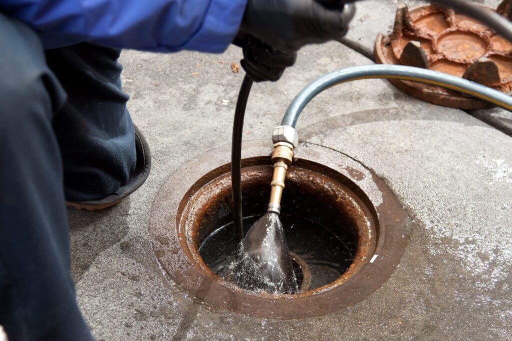 Plumber hydro jetting a sewer line through a manhole in Villa Rica