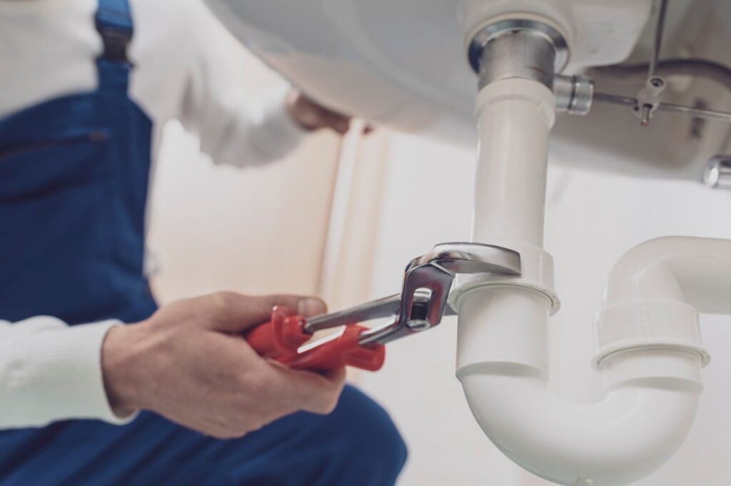 Plumber repairing a white drain pipe beneath a sink in Villa Rica