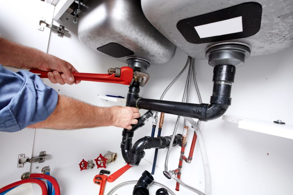 Plumber repairing drain pipes beneath a kitchen sink in Villa Rica